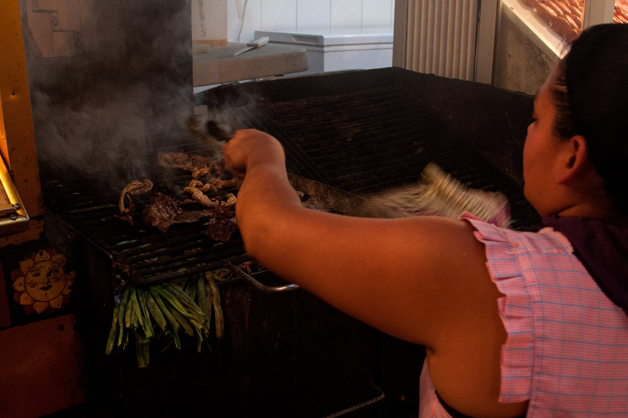 Mujer asando maíz y otros productos en un mercado mexicano